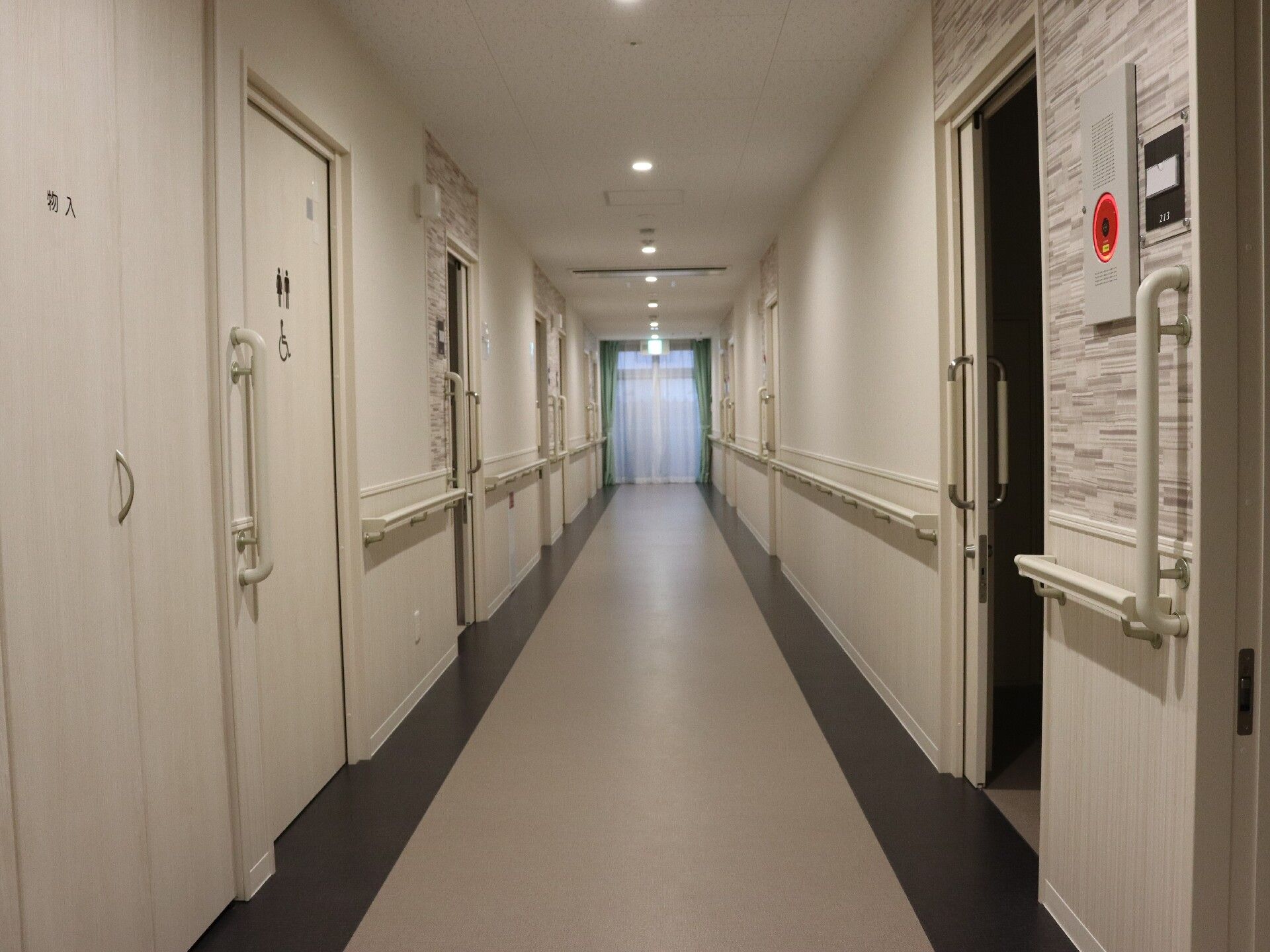 まっすぐに続く廊下に手すりと個室のドアがある様子。施設内の廊下の様子