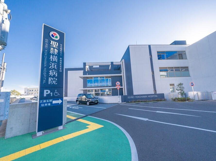 「聖隷横浜病院」と書かれたブルーの館銘板が設置され、道路には黒い車が止まっている。