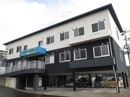 白と黒の外壁の建物は3階建てで、1階部分は駐車場となっていて、たくさんの車が止まっている。