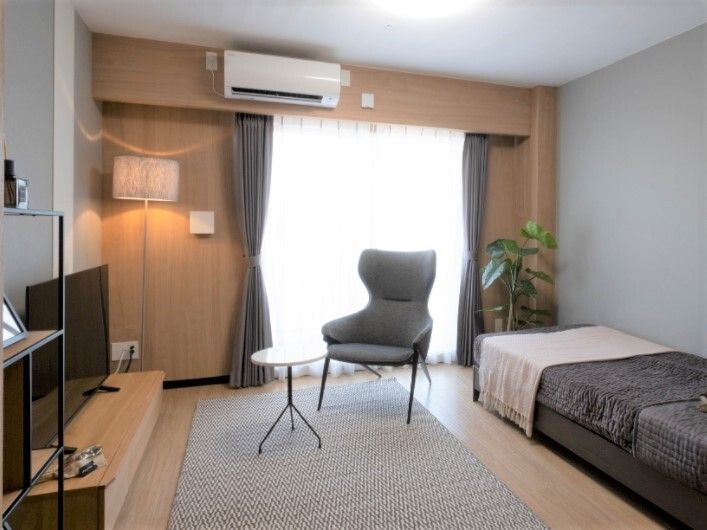 大きな窓が付いたフローリングの部屋にはラグが敷かれ、テーブルセットや寝具付きのベッドがあり、エアコンもついている。