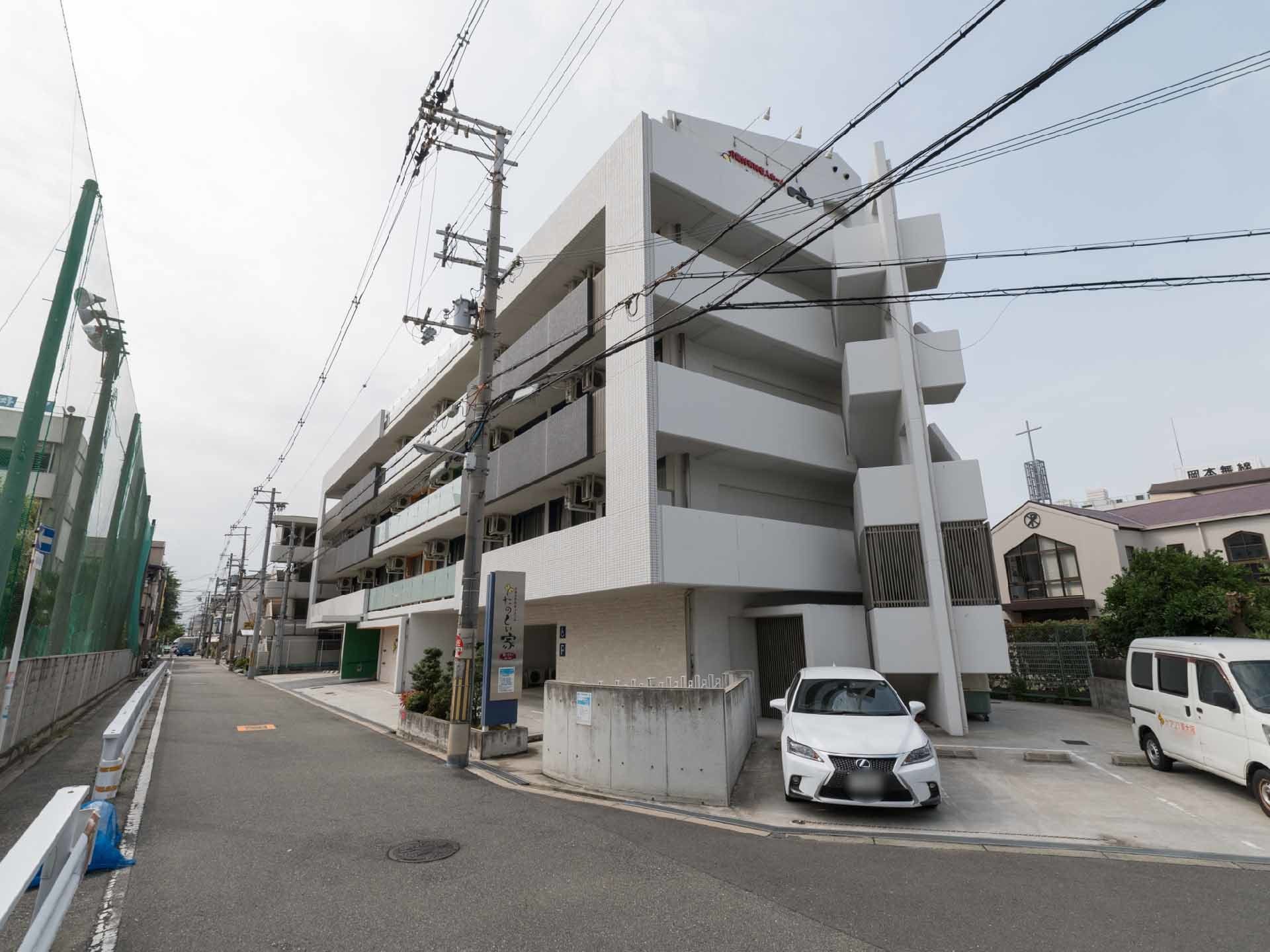 施設の全体像が見えるように写した写真。道路側から撮られている。5階建のビルで、施設前の駐車場は、3台分用意されている。