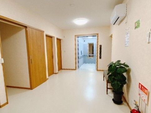 奥にエレベーターがある廊下の様子。左側に個室が並んでいる様子