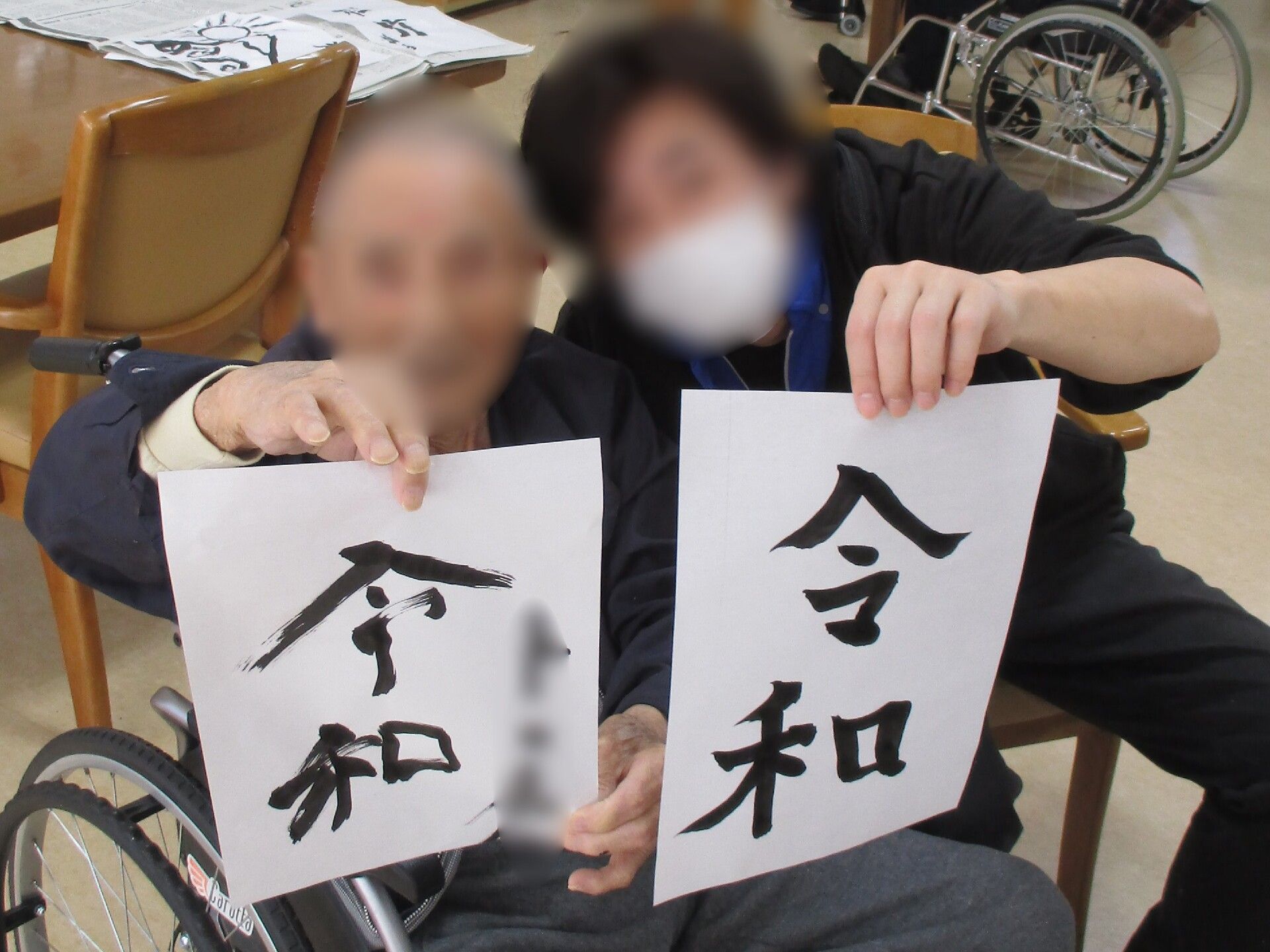 カルテのようなものを見ながら笑顔で話しているブルーのエプロンを付けた若い女性スタッフと高齢女性。