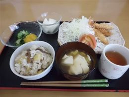 炊き込みご飯やみそ汁、野菜の和え物などが乗った黒いトレーには千切りキャベツが添えられたフライもある。