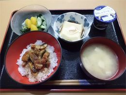 みそ汁やカットしたウナギが乗せられた丼、豆腐や野菜の和え物などが並べられた黒いトレー。