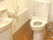 ふたのない便座が付いたトイレが設置されていて、壁には手すりとトイレットペーパーホルダーがあり、手洗い場もある。
