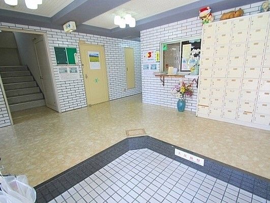 大きな靴箱が置かれた玄関をよく見渡せる位置に受付があり、花や消毒液などが置かれている。左側には階段も見える。