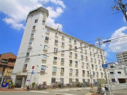 白を基調とした大きな建物が道路に面して建てられていて、建物の周りには木もたくさん植えられている。