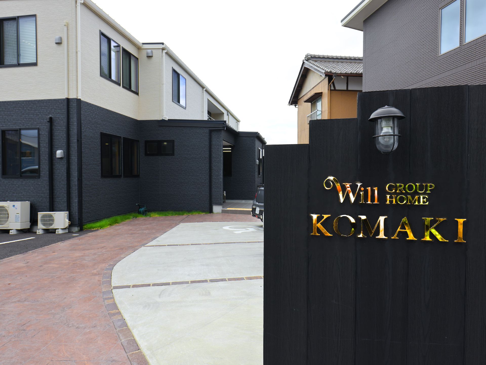 建物の手前にある黒い壁に金色でWill group home komakiと書かれた看板