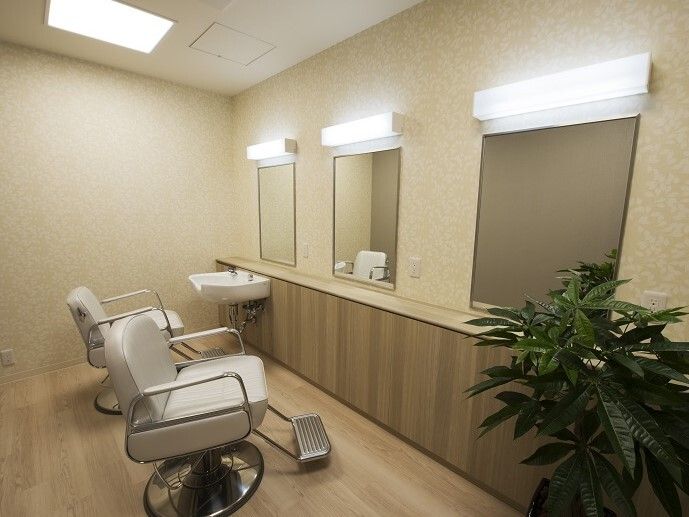 ヘアサロン用の椅子が２脚あり、それぞれの前にはライト付きの鏡が設置されている。一番奥には鏡付きの洗髪台もある。