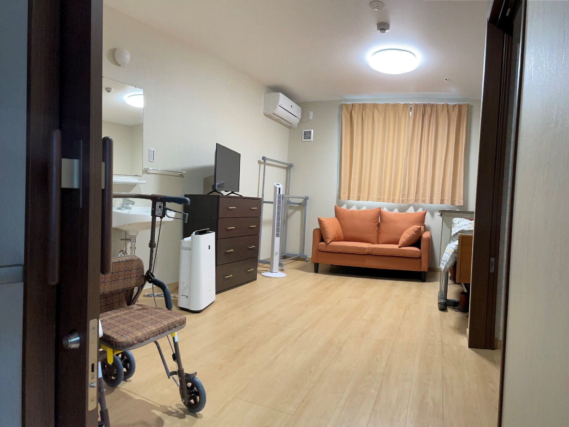 ソファやタンス、ベッドなどがあるフローリングの部屋には洗面所やエアコンが付き、シルバーカーも置かれている。