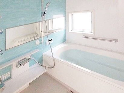 大きな一人用の浴槽が設置された浴室は白とライトブルーでまとめられ、壁には大きな鏡とシャワーが付いている。