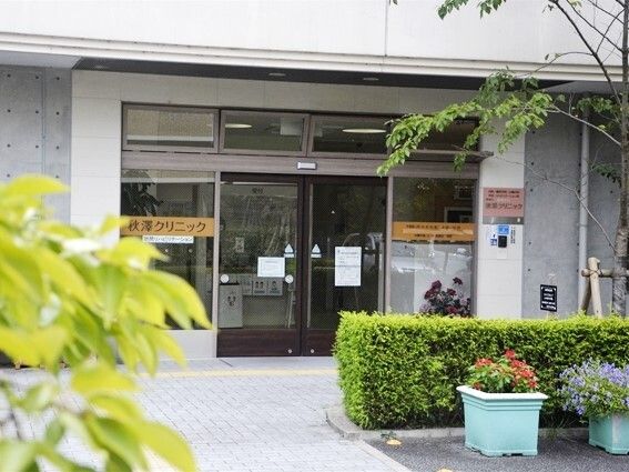 木や花が周りに植えられていて、点字ブロックが敷かれた場所にあるクリニック。自動ドアにはクリニック名が書かれている。