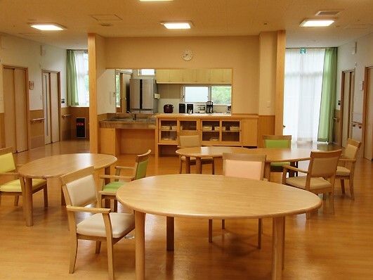 対面式のキッチンが付いたダイニング。円形のテーブルセットが複数置かれ、白やグリーンの椅子がセットされている。
