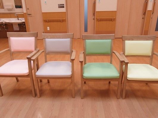 ピンク、グリーン、イエロー、ラベンダー色の椅子が並んでいる。それぞれの椅子には肘置きがあり、奥には洗面所がある。
