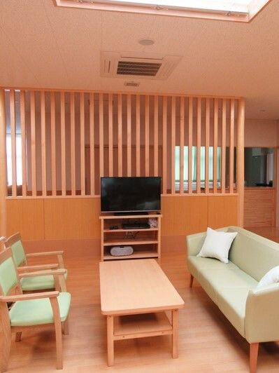 木製のテーブルをはさんでクッションが添えられたソファといすが置かれいて、正面にはテレビも設置されている。