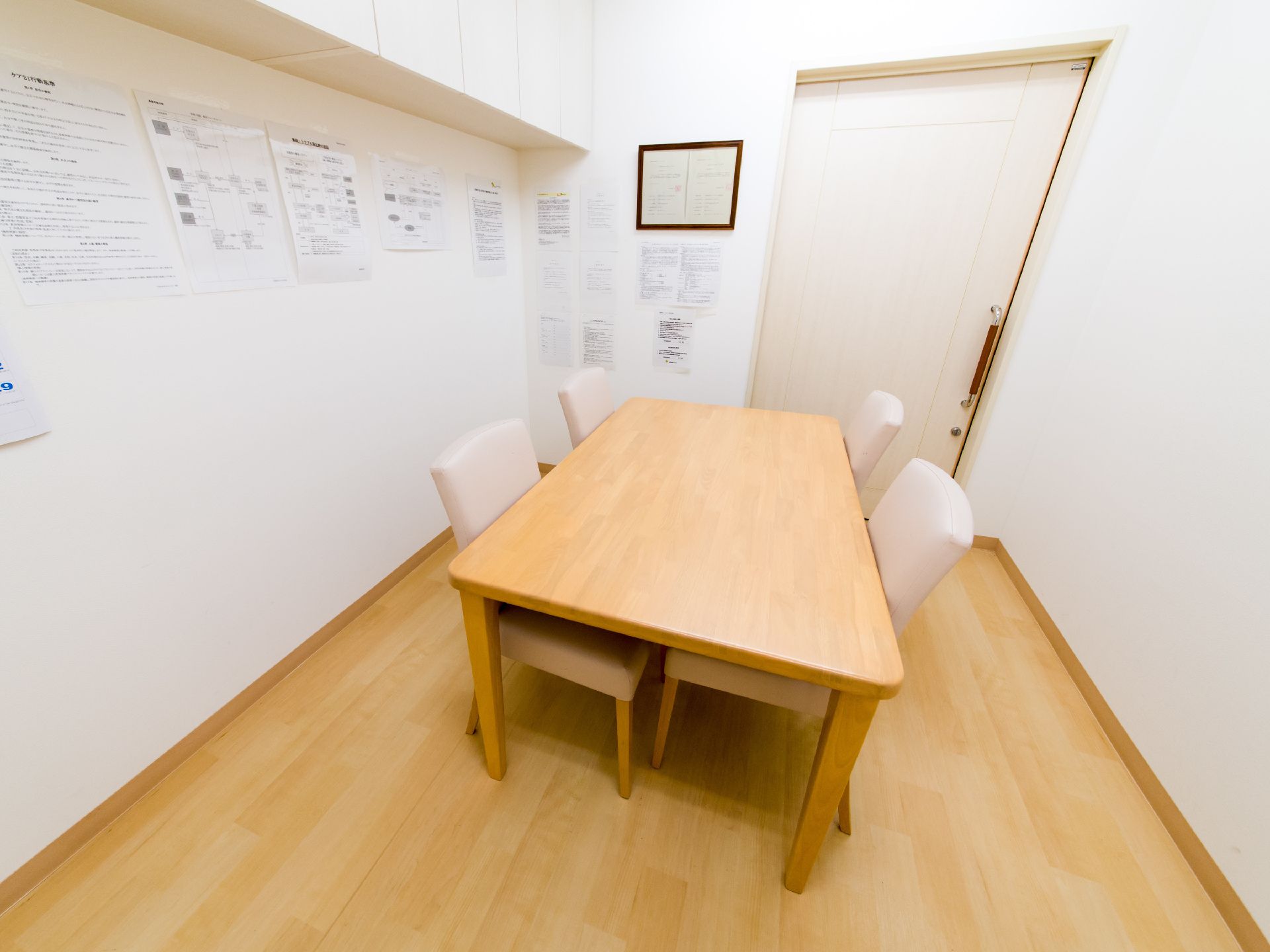 4人で利用できる面談室は、床のフローリングとテーブルの色が同じ色に統一されている。出口に向かって左側の壁には、掲示物がたくさんある。
