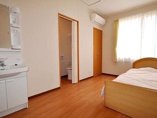 エアコンや寝具付きのベッド、洗面所、トイレがあるフローリングの部屋には大きな窓が付いている。