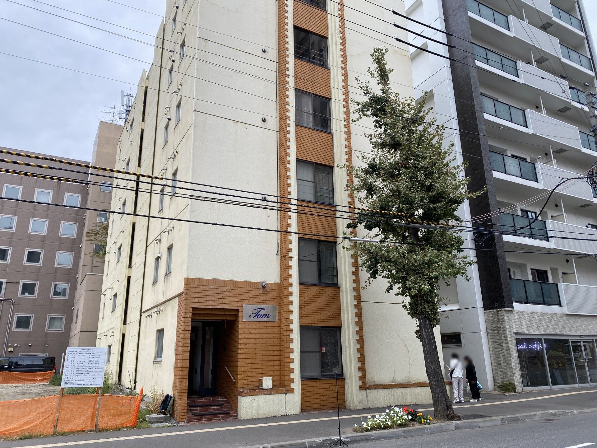白い服を着た高齢女性が車いすの高齢男性のそばに立ち、二人は笑いながら話をしている。