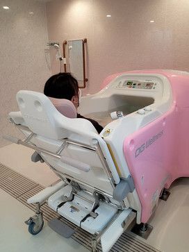 男性がピンクと白の座ったまま浴槽内に移動できる機械浴内に入っている。奥にはシャワーもある。