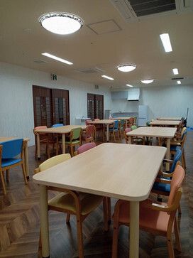 木製のダイニングテーブルが複数置かれた食堂。テーブルには赤や黄色、ブルーなどの椅子がセットされている。