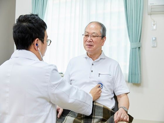 なにかを見て笑顔で手をたたいている高齢女性とスタッフの様子。施設での一場面の写真