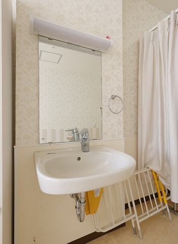 ピンクのエプロンを付けた若い女性スタッフが車いすの高齢女性の手に自分の手を重ね、笑顔で接している。