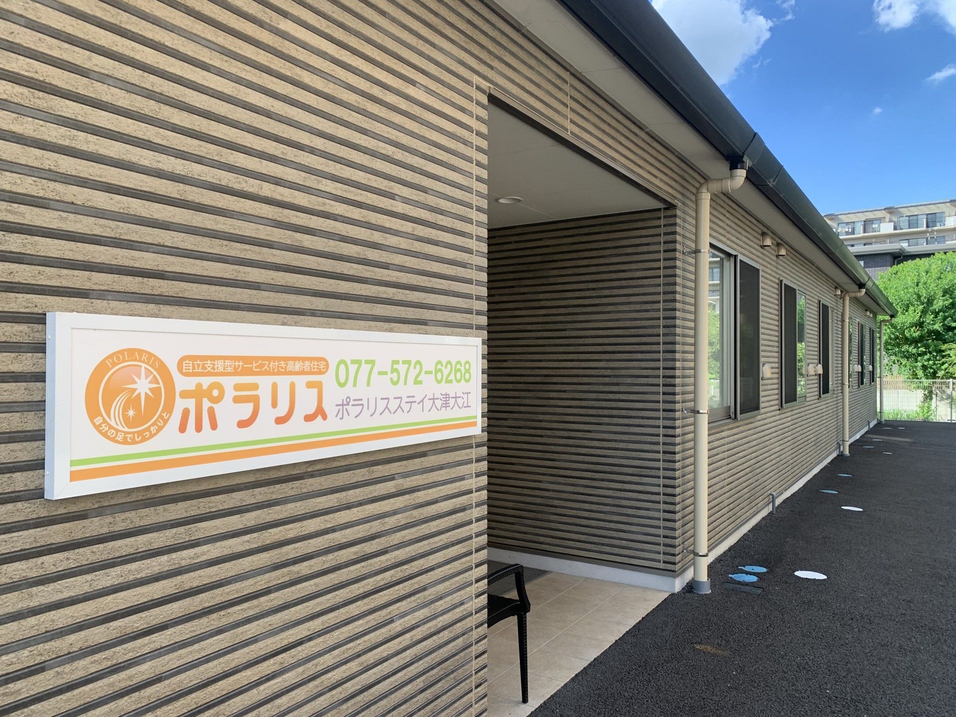 車いすの高齢男性と白いゆったりとした服を着た高齢女性が笑顔で話している。