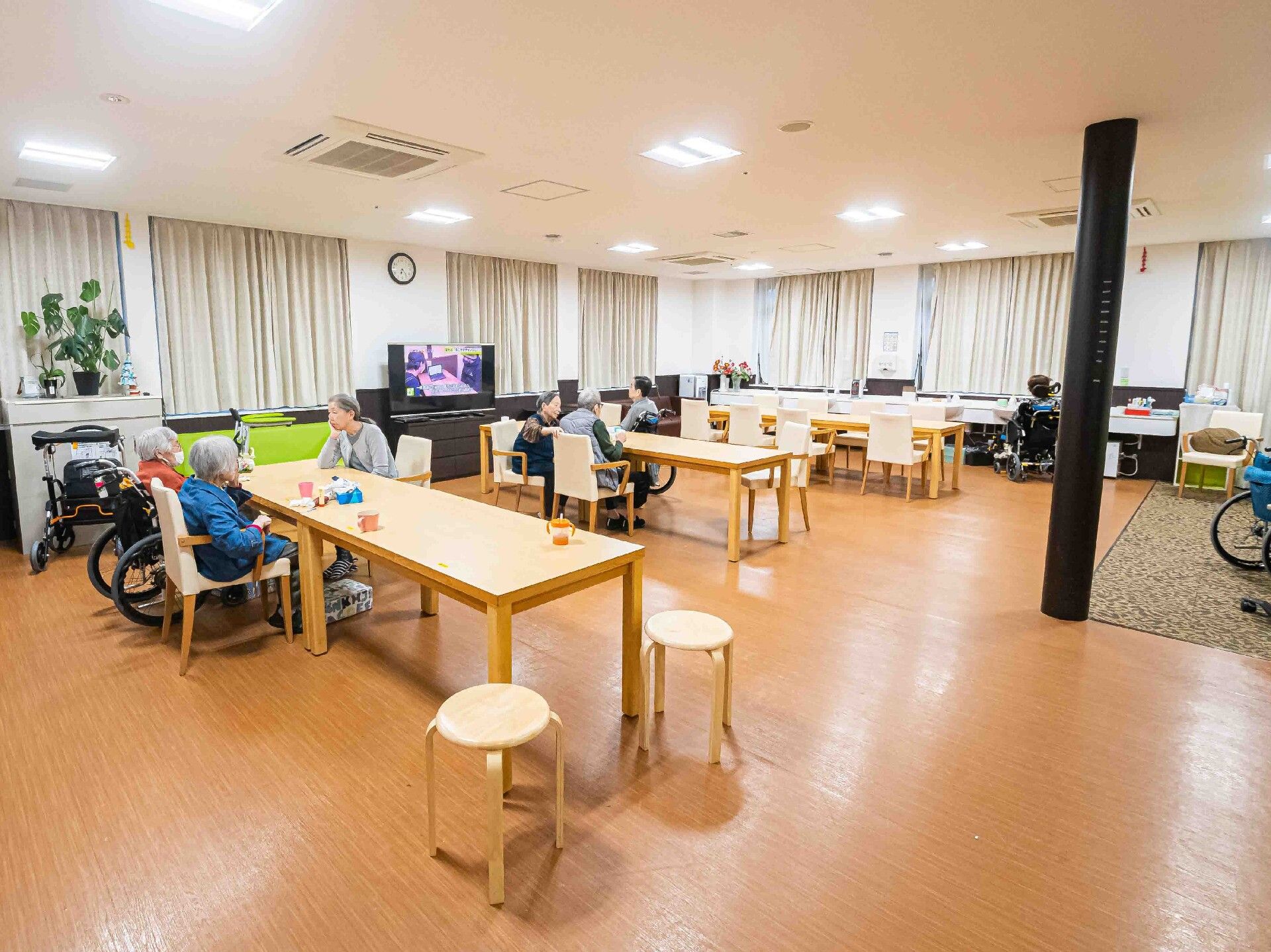 複数のダイニングテーブルセットが置かれたリビングダイニング。複数の高齢者が席に付いている。