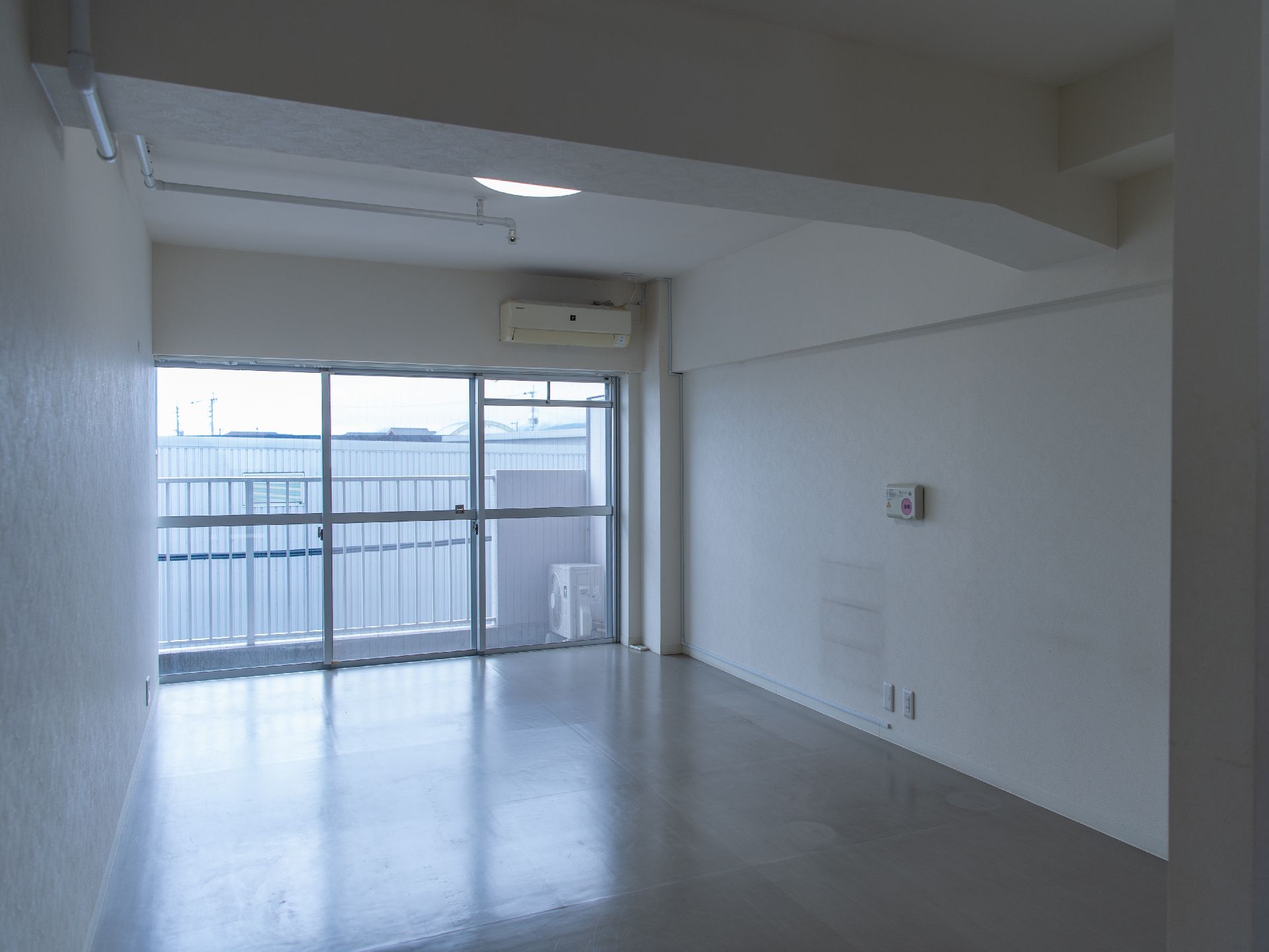 壁一面が窓ガラスの白い壁の何も置かれていない部屋