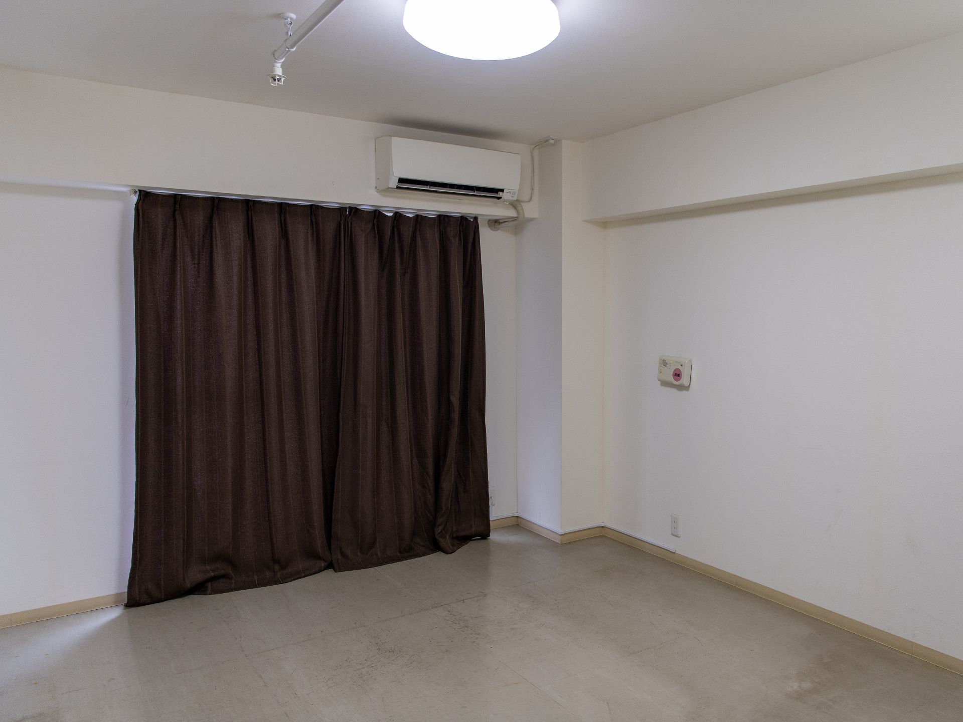 エアコンが白い壁についている黒いカーテンで窓が覆われた何も置かれていない部屋