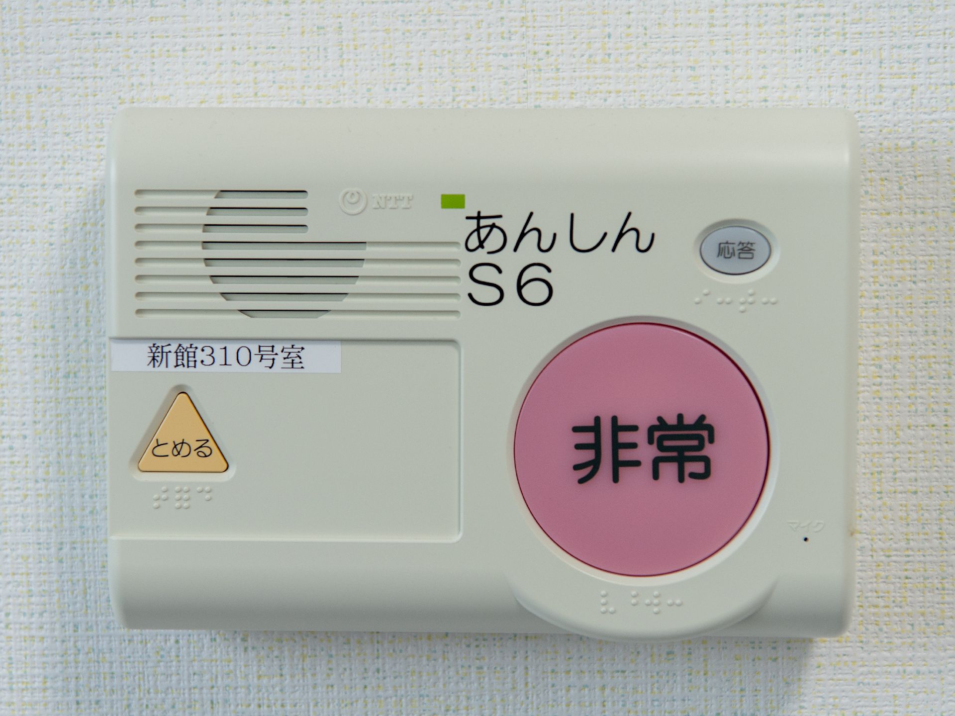 白い壁に取り付けられた非常と書かれた赤いボタンが付いている四角い機械