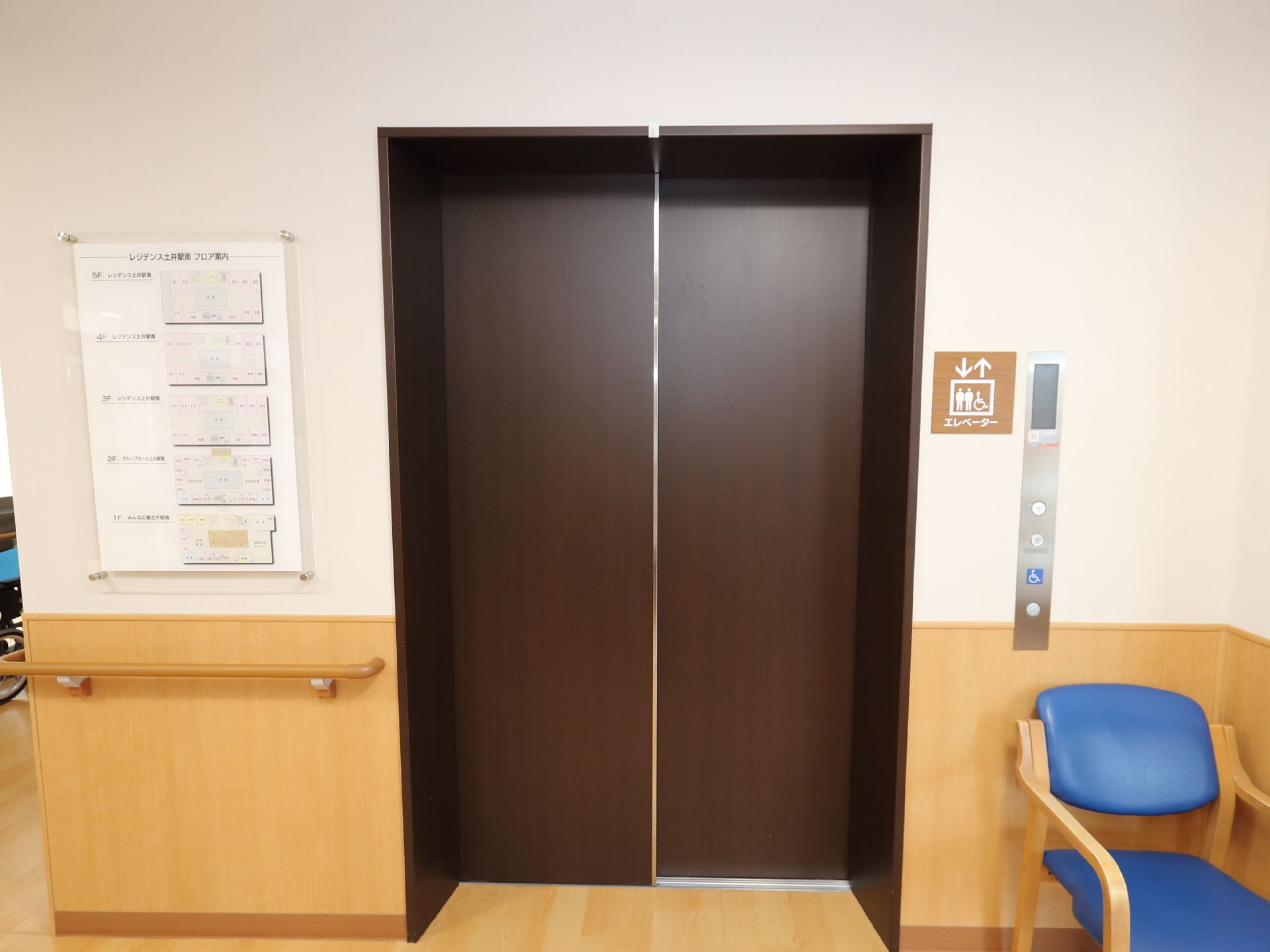 屋外でピンクのエプロンを付けた若い女性スタッフに車いすを押してもらいながら散歩を楽しんでいる高齢女性。