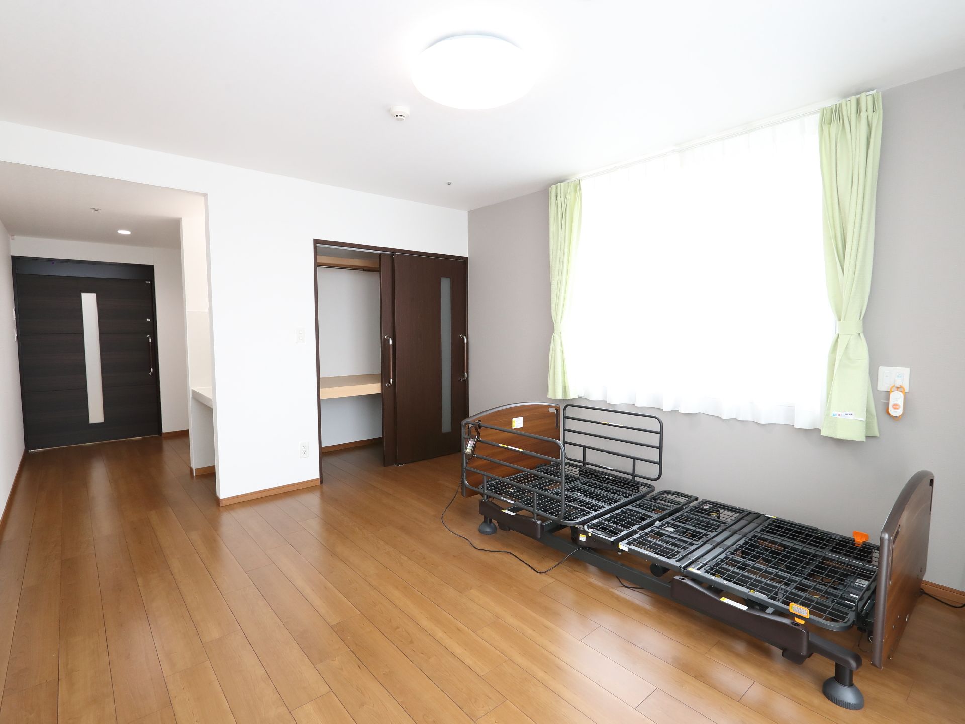 カーテンに遮られた大きな窓ガラスがあるベッドが置かれた白い壁の部屋