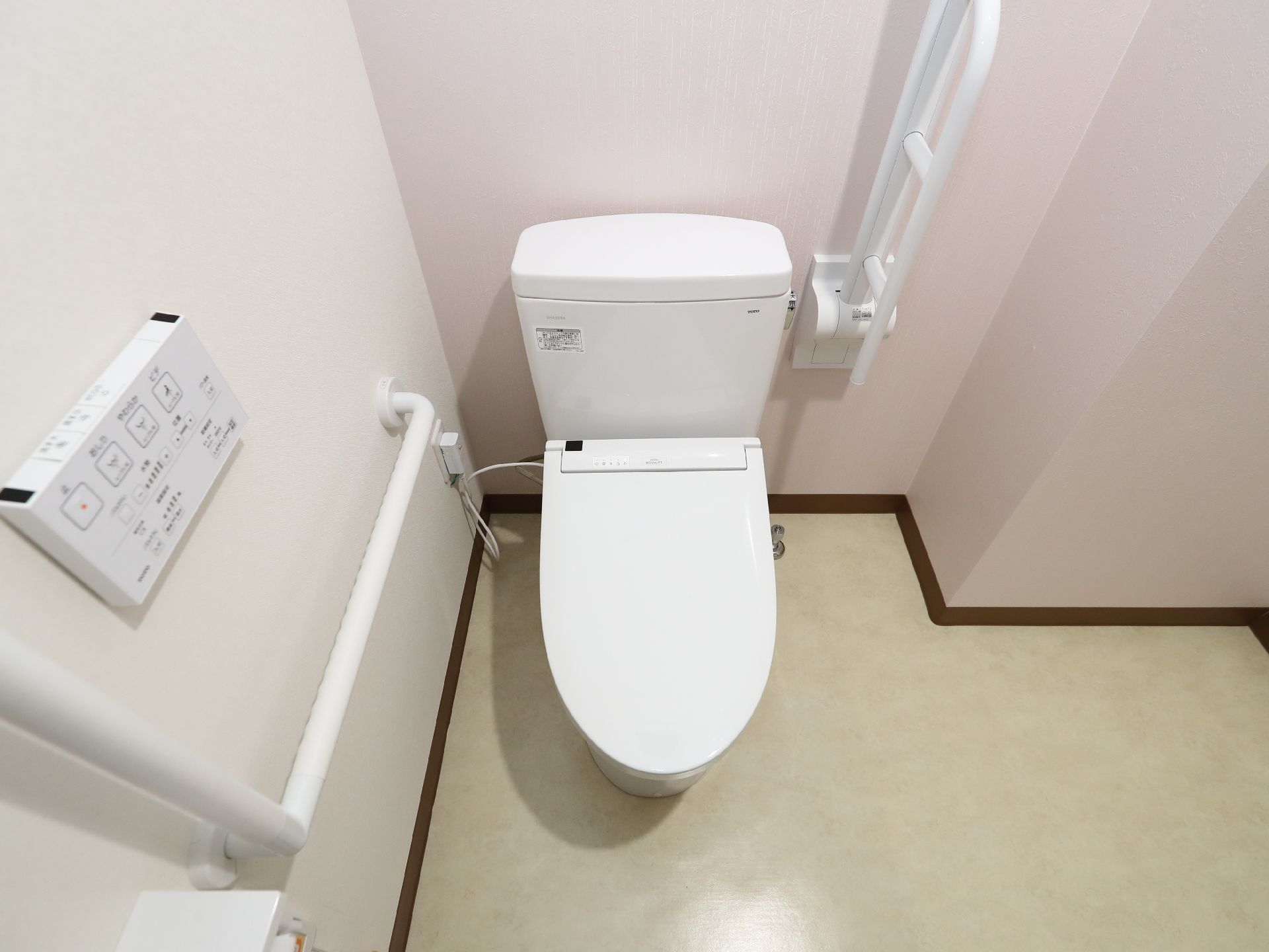 手すりが付いた白い壁際に配置された蓋のしまった洋式便器