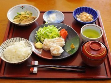 一人分の食事が用意されている。赤い角盆に、ご飯や汁物・主菜・副菜数点に加え、緑茶がのっている。箸には箸置きが添えられている。