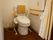 洋式トイレが設置された横の壁には、Ｌ字型の手すりとナースコールが設置されている。天井にカーテンが取り付けられている。