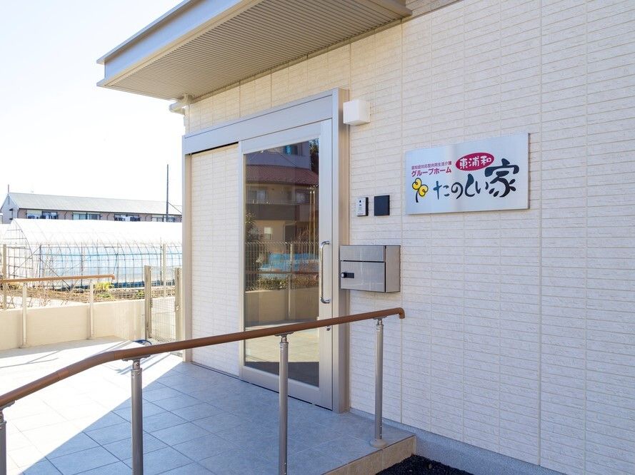 手すり付きのスロープが付いた玄関にはポストやインターフォンが設置され、ホーム名が書かれた表札もある。