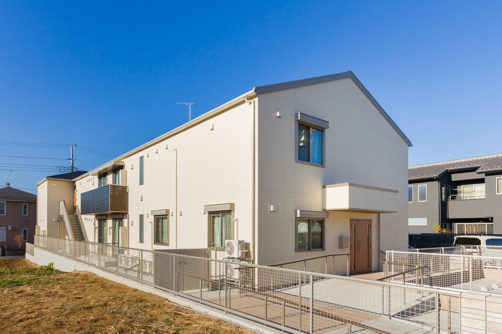 アイボリー色の外壁がアットホームな雰囲気の2階建ての建物。駐車場も建物の前に用意されている。