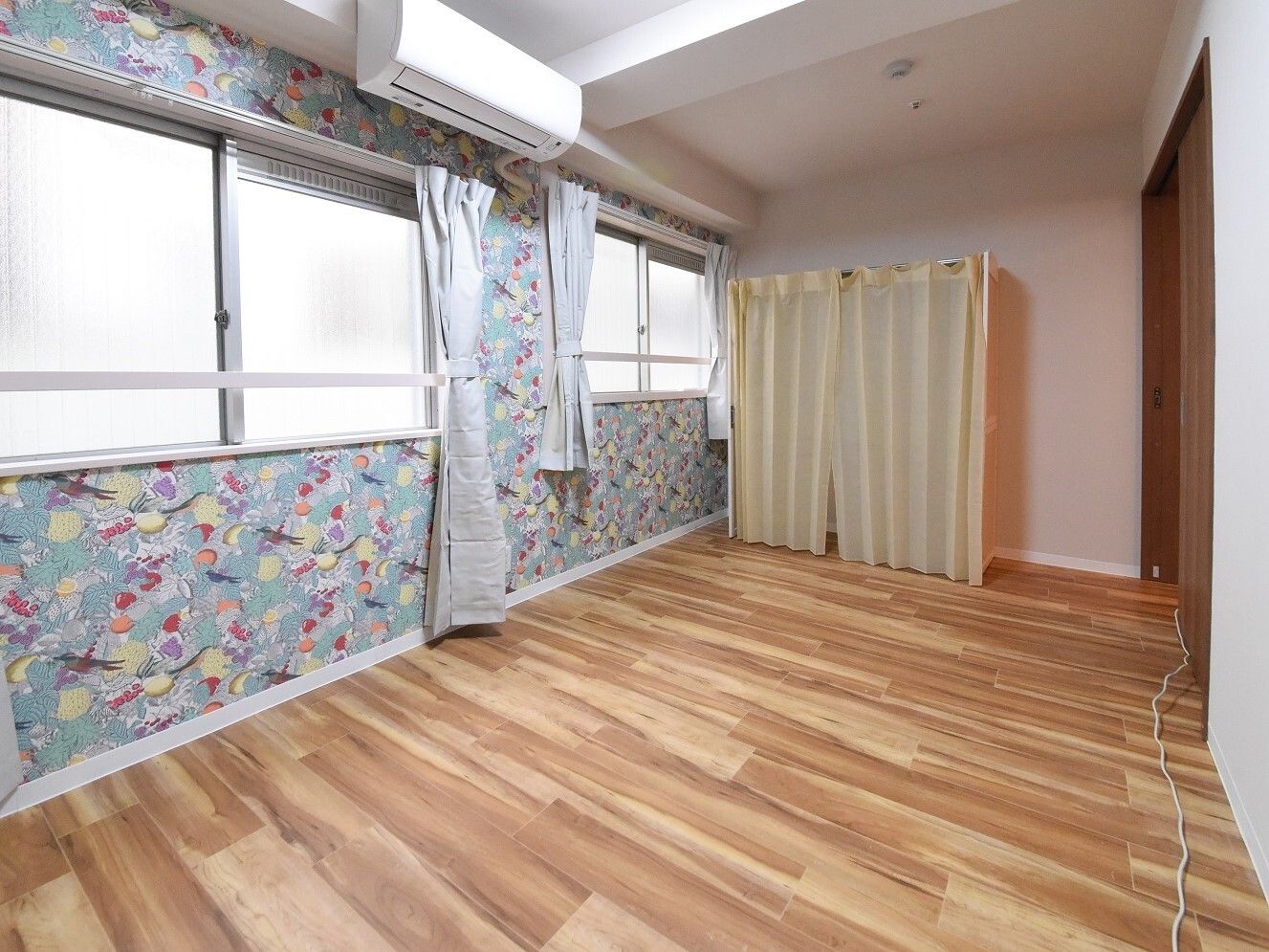 カーテンで開け閉めするタイプの収納が付いたフローリングの部屋。窓の大きさに対してとても長いカーテンが付いている。