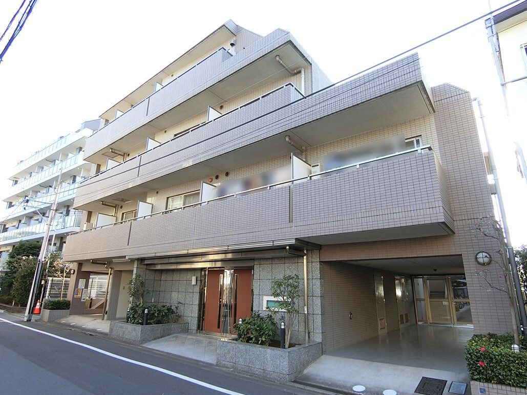 ブラウン系の建物は各フロアにベランダが付き、玄関の両サイドに花壇があり、1階部分の一部は駐車場になっている。