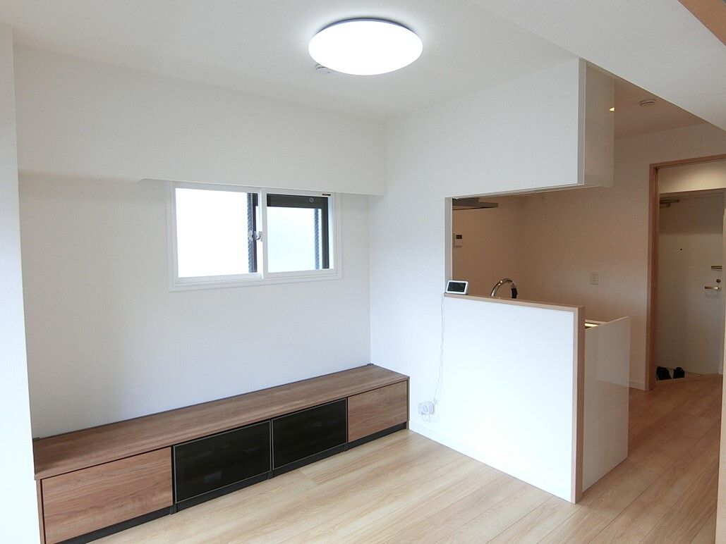大きなテレビボードが設置されたフローリングの部屋には対面式のキッチンがあり、小さな窓が付いている。