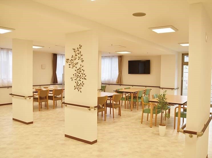 少人数向けのダイニングテーブルが複数並んだ食堂にはたくさんの窓があり、壁には手すりとテレビが付いている。