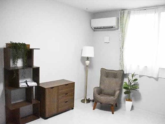 エアコン付きの部屋にはいすやラック、観葉植物が持ち込まれ、窓にはレースカーテンとカーテンが付いている。