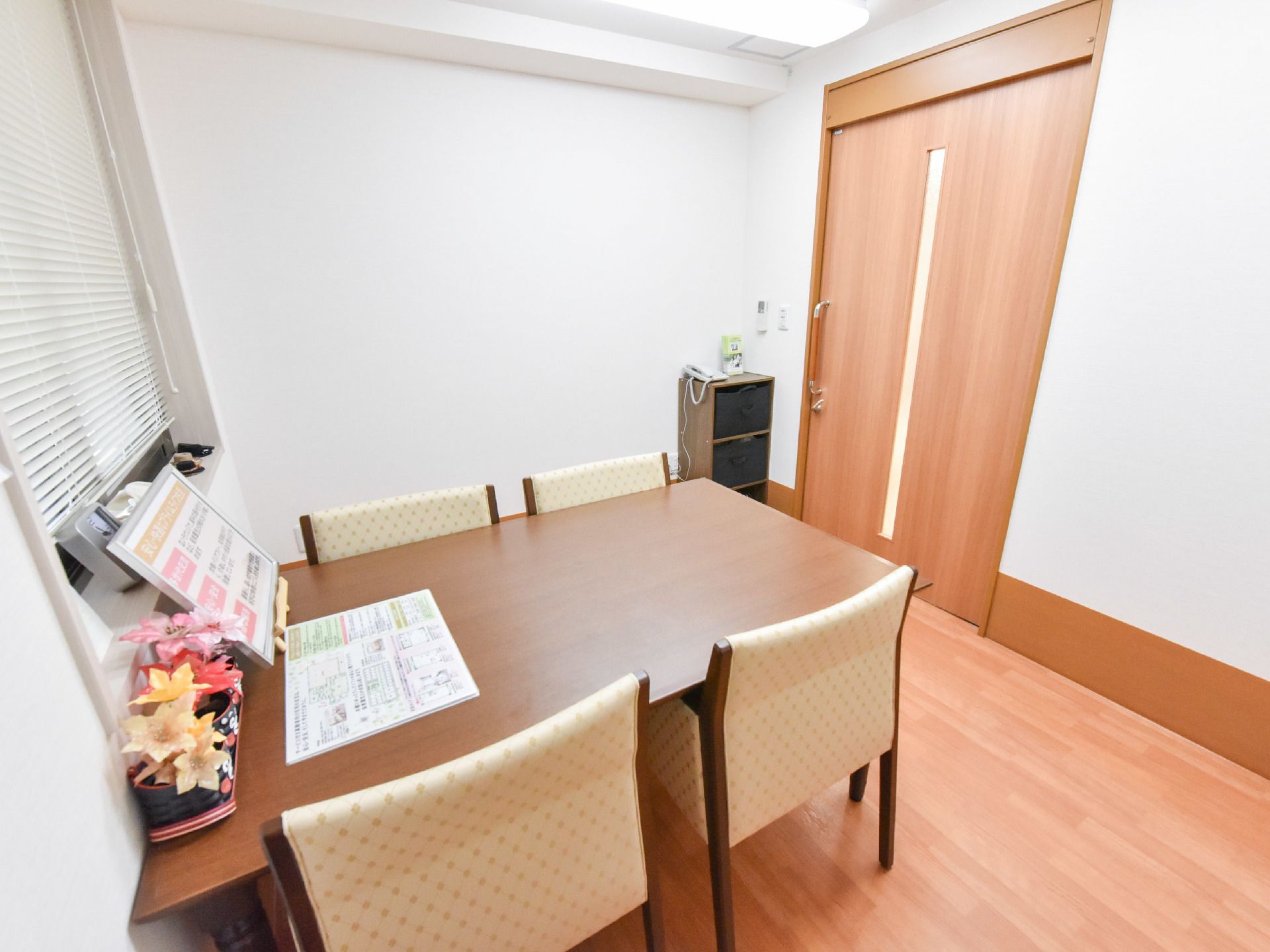 応接室の扉は横開きタイプ。テーブルが1つあり椅子が4つ。資料などが置かれている。内線電話も設置されている。