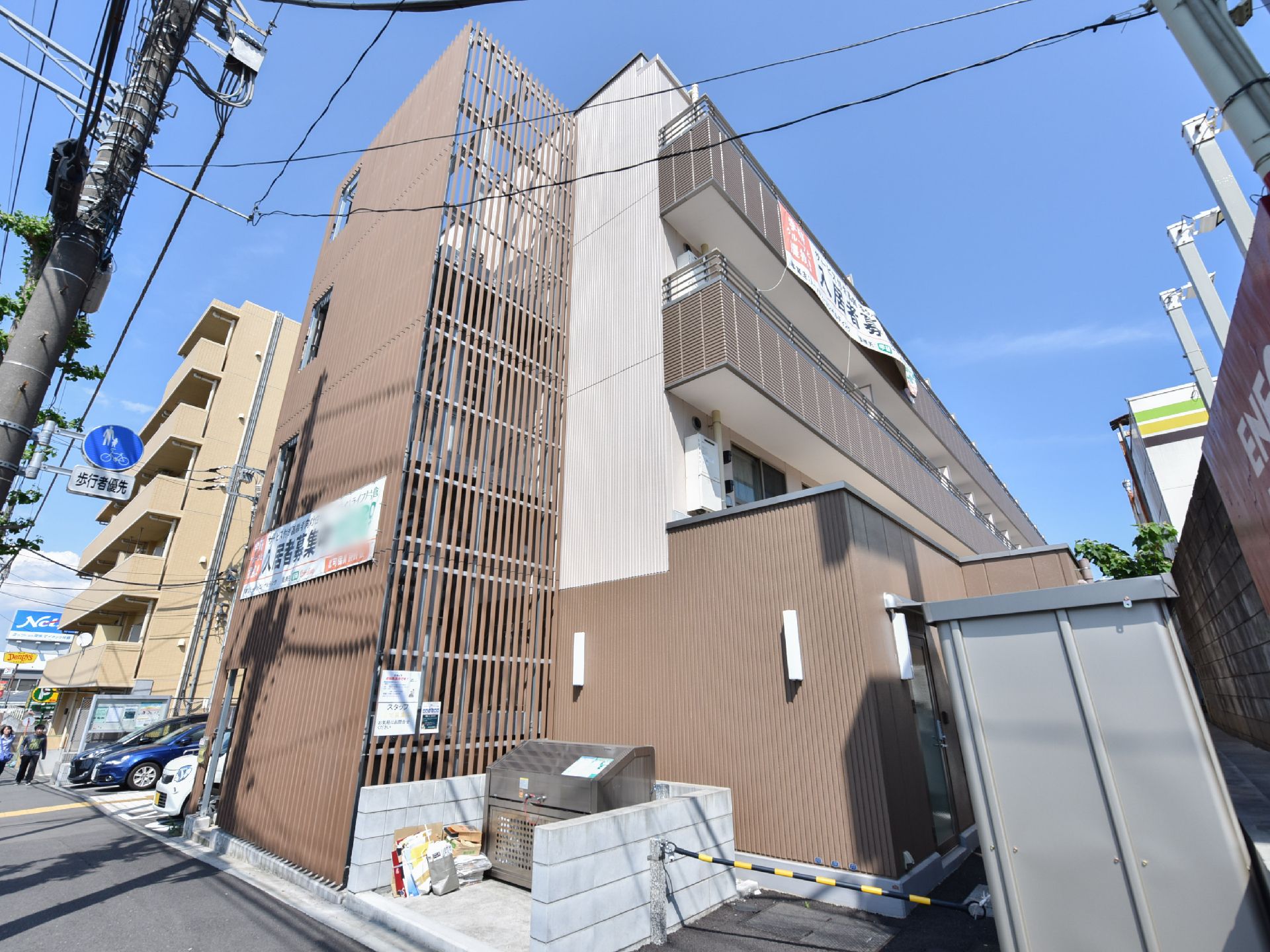 施設入り口の横には非常階段が設置されている。隣にはゴミ集積場がある。2階以上にはベランダがあるのが見える。