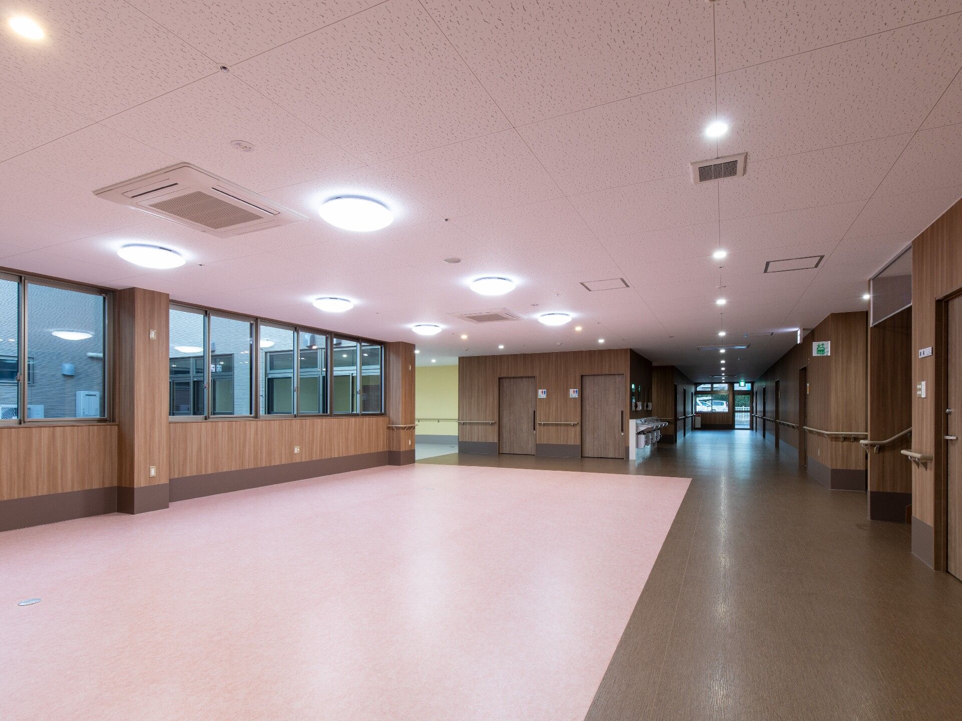 ピンクのフロアの食堂には家具などは置かれていない。右側にはまっすぐな廊下があり、手すりが付いている。
