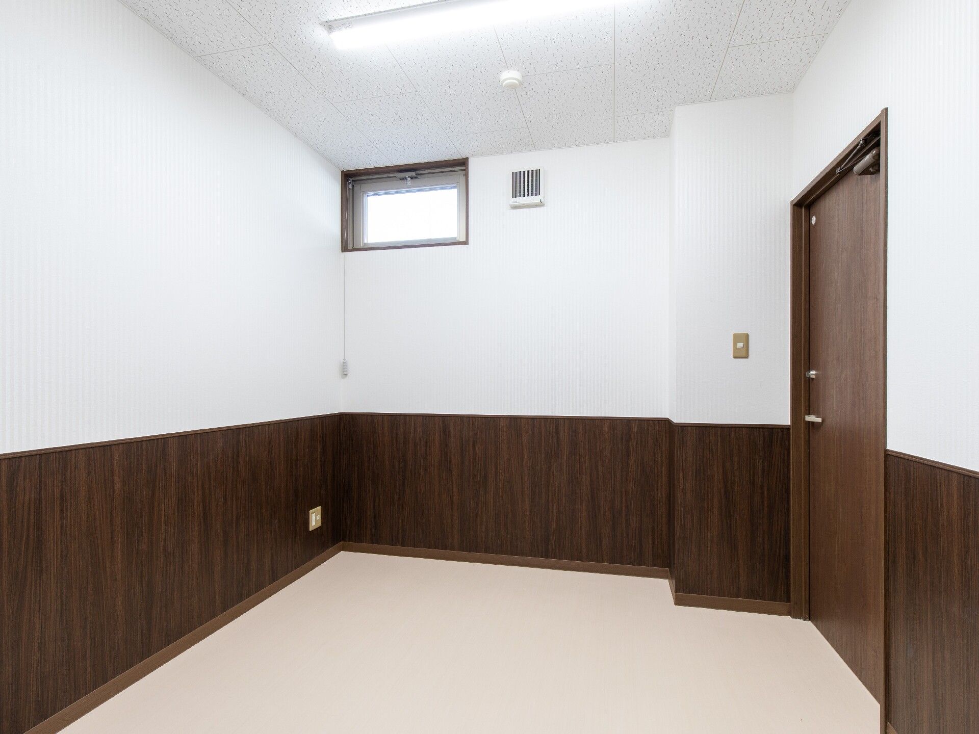 小さな小窓が付いた部屋には家具は置かれていない。壁の半分が白で、もう半分がブラウン。