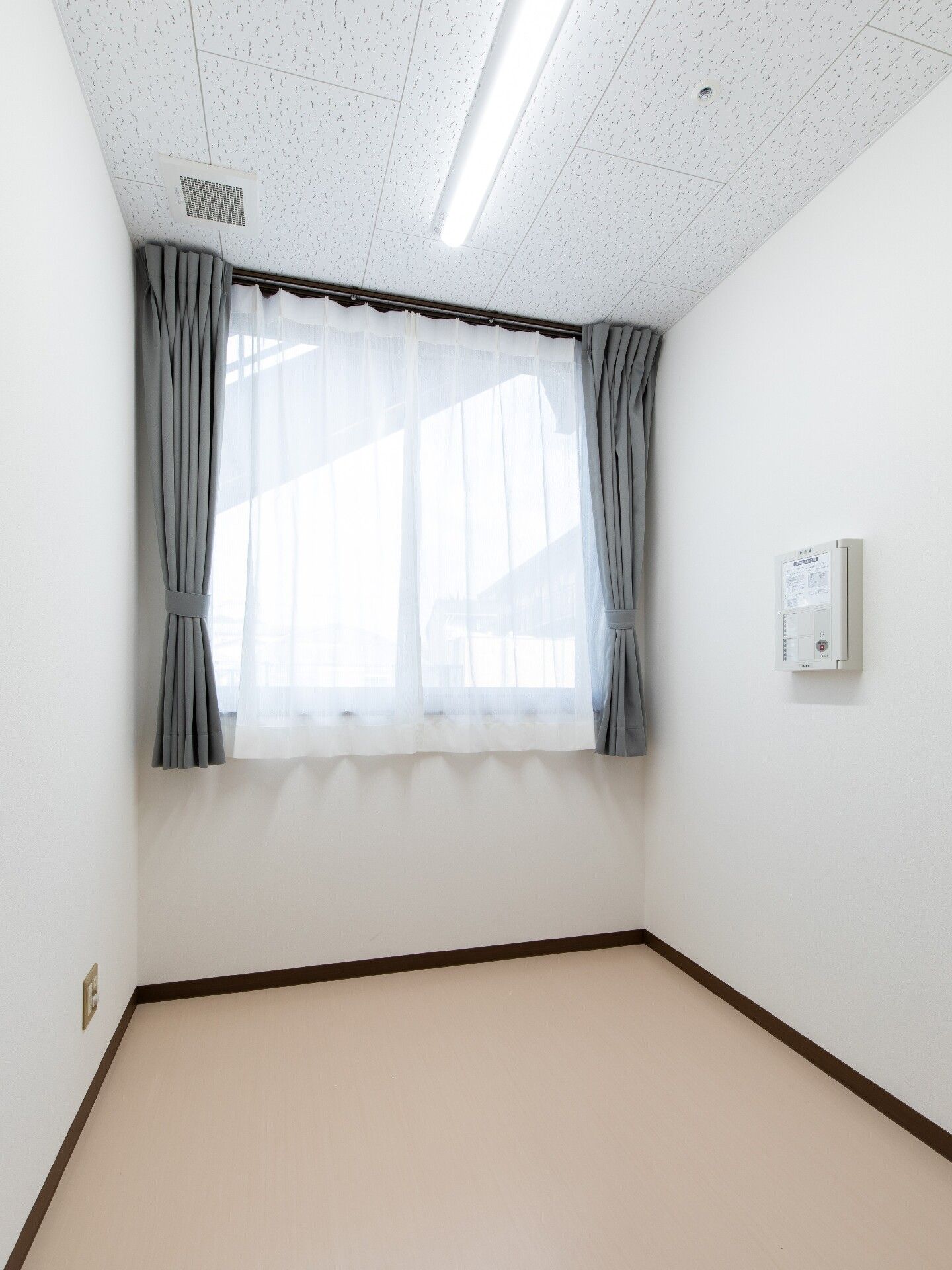 レースカーテンとカーテンが付いた窓があるシンプルな部屋には家具は置かれていない。