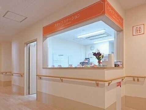 車いすに乗る女性と笑顔でそれを押すスタッフ。二人で散歩しながら会話している様子